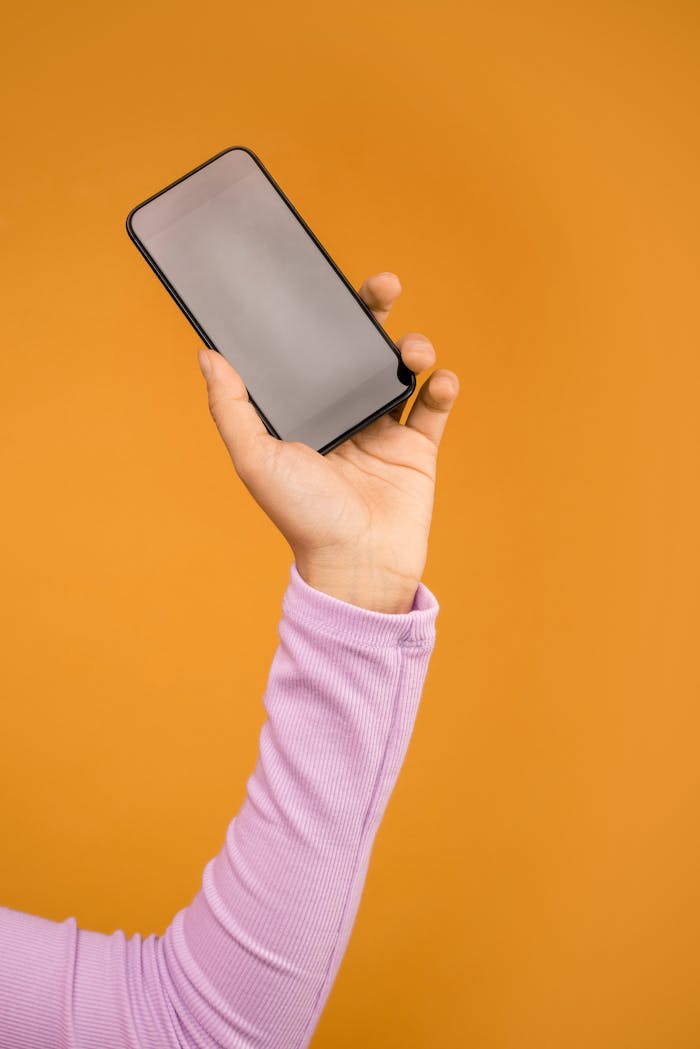 Close-up of a hand holding a smartphone against an orange background.